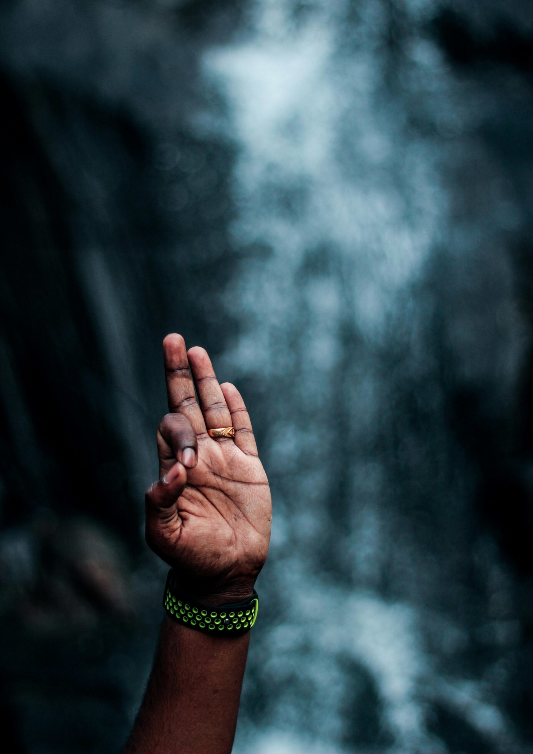 A close-up of a hand gesture in front of a blurred waterfall in Wayanad, India.