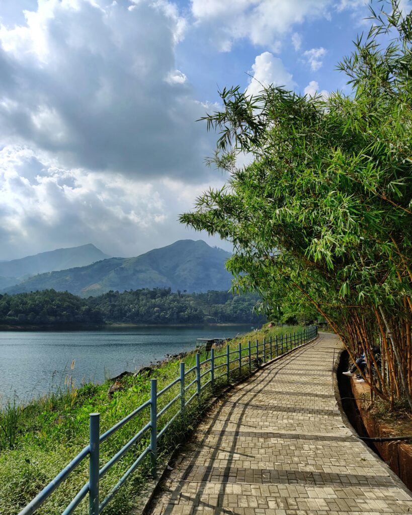 A Walk Through the Edakkal Caves: Mysteries in Stone – Your Ultimate Wayanad Travel Guide Tranquil bamboo-lined walkway by Padinjarathara Dam with stunning mountain views.